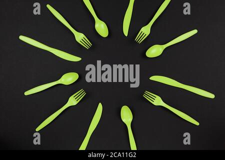 Biodegradable reusable recyclable green forks, spoons, knifes made from corn starch or oats laid out like sun or flower on black background. Eco, zero Stock Photo