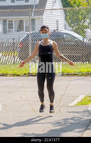 A fit Asian American young lady wearing a mask jumps rope as part of a rigorous workout on a hot summer morning. In Flushing, Queens, New York City.