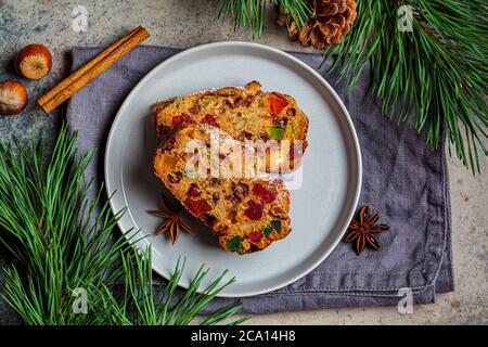 Piece of Christmas fruit cake on a plate in festive decorations, top view, dark background. Stock Photo