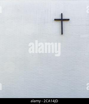 Metallic cross on a white new plastered brick wall, viewed from  front. Generic church wall exterior. High resolution textured background, copy space. Stock Photo
