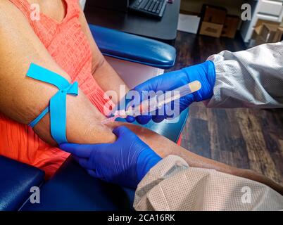 With the Corona lab tech wears mask, face shield, gloves, and disposable gown to take a blood sample from patient eho is also wearing a mask. If you think you have the virus will you go see a doctor? Stock Photo