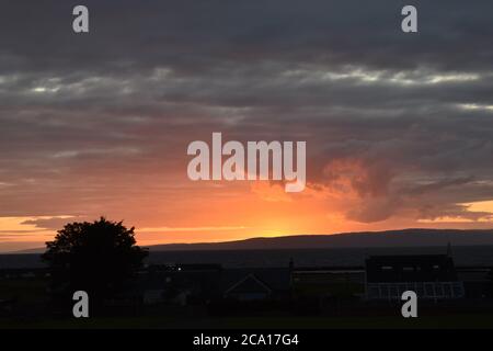 The face in the clouds appears to be blowing the sun over the horizon. Stock Photo