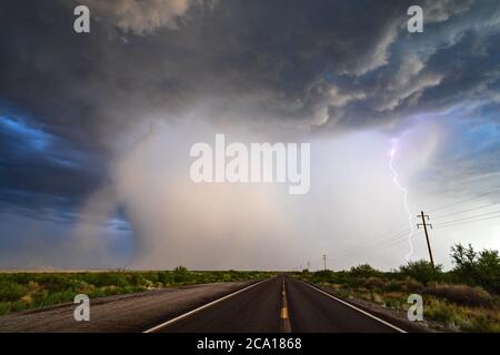 Road leading to a powerful monsoon storm with dramatic clouds, heavy rain and lightning over the Willcox Playa in southeastern Arizona Stock Photo