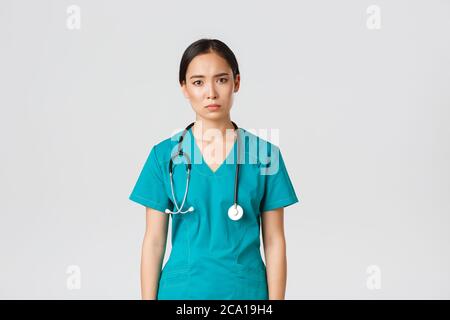 Covid-19, healthcare workers, pandemic concept. Exhausted young asian female nurse, doctor looking tired after shift in hospital, looking sad with Stock Photo