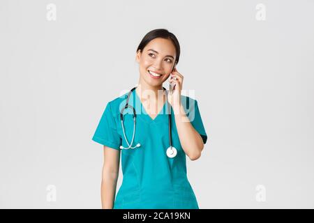 Covid-19, healthcare workers and preventing virus concept. Pretty smiling asian female doctor, physician in scrubs having conversation, talking on Stock Photo