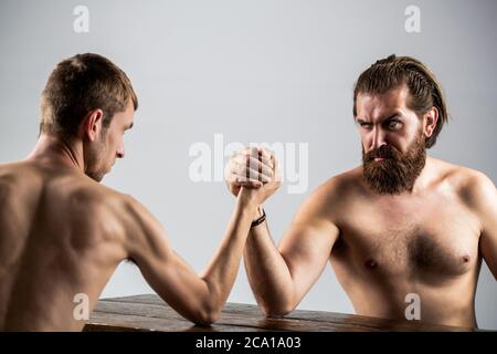 Arm wrestling. Heavily muscled bearded man arm wrestling a puny weak man. Arms wrestling thin hand, big strong arm in studio. Two man's hands clasped