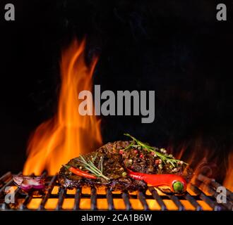 Beef steaks on the grill grate, flames on background. Barbecue and grill, delicious food. Stock Photo