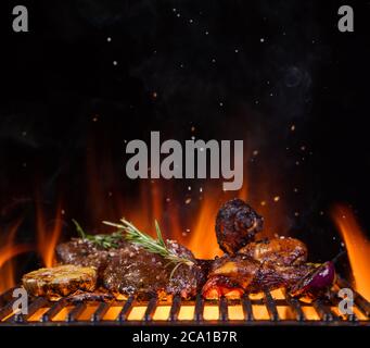Beef steaks with vegetable on the grill grate, flames on background. Barbecue and grill, delicious food. Stock Photo