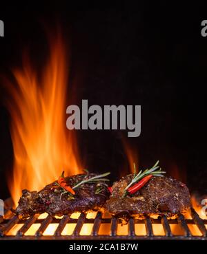 Beef steaks on the grill grate, flames on background. Barbecue and grill, delicious food. Stock Photo