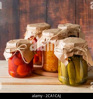 Pickled farm vegetables in glass jars on a wooden background. Fermented trending food. Home rustic style. Stock Photo