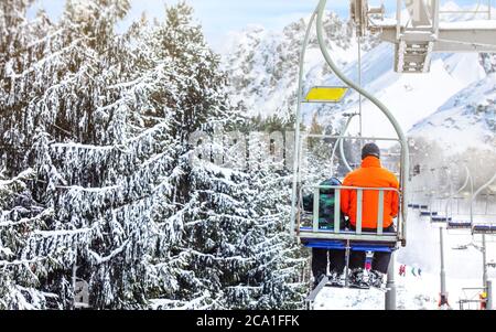 Skiers on chair lift, piste under, snow covered trees on right side Stock Photo