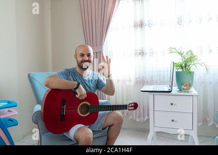 Young musician sitting on sofa with guitar in hand. TURKEY Stock Photo