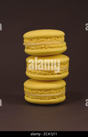 Three tasty french yellow colored macarons on the brown background. Colorful macarons. Front view. Stock Photo