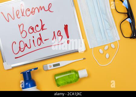 Welcome back covid-19. Liquid antibacterial soap, antiseptic gel bottle, medical pills, face mask and eyeglasses on the yellow. The second wave of Stock Photo