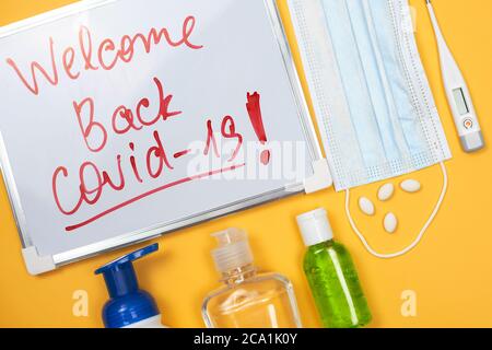 Welcome back covid-19. Liquid antibacterial soap, antiseptic gel bottle, medical pills, face mask and eyeglasses on the yellow. The second wave of Stock Photo