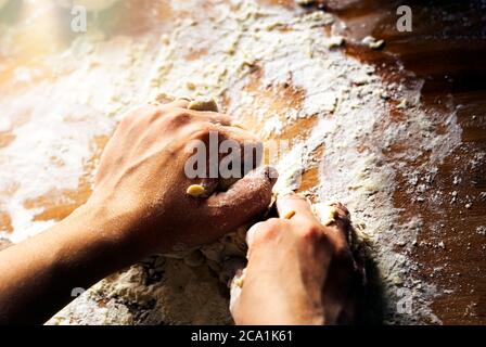 female hands kneading a flour dough by rolling it on a wooden board. Preparation of flour-based food such as bread or pizza Stock Photo