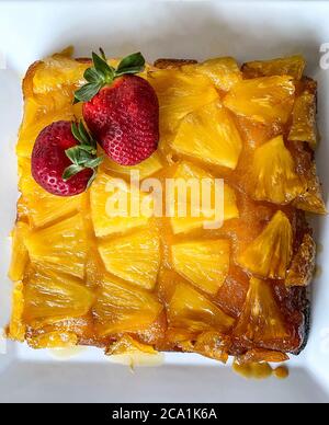 Upside-down pineapple cake decorated with red whole strawberries on a serving plate Stock Photo