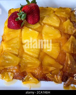 Upside-down pineapple cake decorated with red whole strawberries on a serving plate Stock Photo