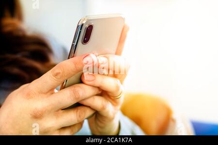 the hands of a young caucasian brunette woman while holding a smartphone typing on the touch screen. Technology and mobile connection. Stock Photo