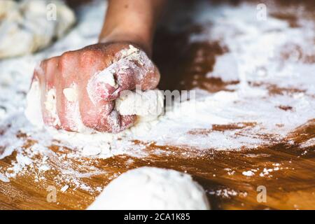 female hand kneading a flour dough by rolling it on a wooden board. Preparation of flour-based food such as bread or pizza Stock Photo