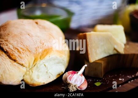 a loaf with a clove of garlic and a slice of parmesan cheese in the background resting on a wooden cutting board. Rustic home kitchen. Homemade food p Stock Photo