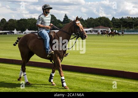 Egham, UK. 3rd August, 2020. A groom wearing a face covering to protect against coronavirus rides a horse along the side of a polo field during a Cartier Queens Cup 2020 league phase match between Next Generation and Segavas at the Guards Polo Club in Windsor Great Park. Next Generation won the match 11-9. Credit: Mark Kerrison/Alamy Live News Stock Photo