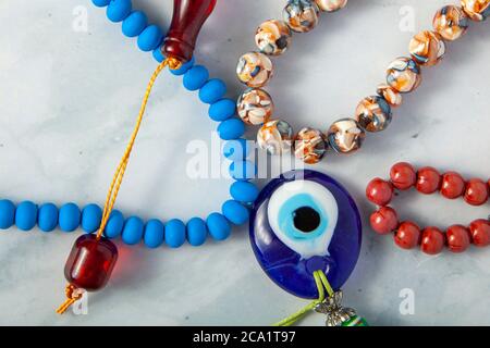 A random collection of a variety of prayer beads (tesbih) arranged on marble background. There is an evil eye amulet in the middle that according to T Stock Photo
