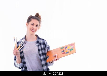 Beautiful young woman holding a painter palette and an assortment of paintbrushes on a light background. Artistic concept. Stock Photo