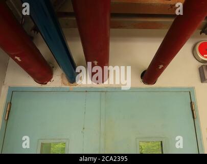 Selective focus on part of water pipes installed above closed door and run through the wall into pump room, the red pipes are used for fire fighting Stock Photo