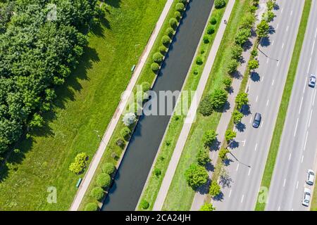 suburban landscape with green trees, lawn and water canal near city road. aerial top view in sunny summer day Stock Photo