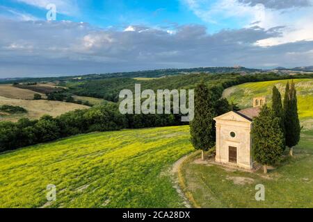 Iconic Tuscanian landscape, with a tiny ancient chapel surrounded by cypresses, under a blue summer sky with sparse clouds Stock Photo