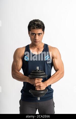 young man wearing gym clothes lift the dumbbell with both hands looking at the camera Stock Photo