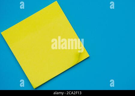 Bright yellow posted note on bright blue flat lay background for education or business organization and reminder concepts. Stock Photo