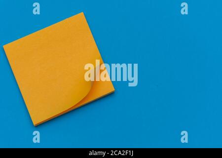 Bright orange posted note on bright blue flat lay background for education or business organization and reminder concepts. Stock Photo