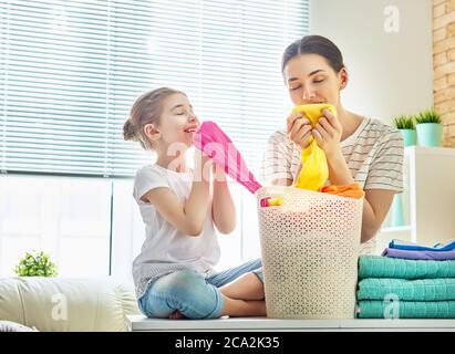 Beautiful young woman and child girl little helper are smelling clean clothes and smiling while doing laundry at home. Stock Photo