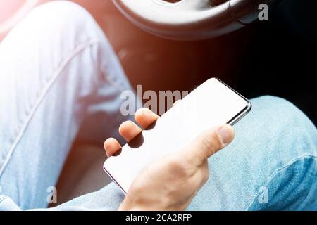Male hand using smartphone in car. Man driving a car. Smartphone in a car use for Navigate or GPS. Mobile phone in driver hand. Stock Photo