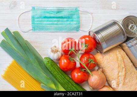 Donations food, vegetables, bread, pasta, canned food, and medical protective mask on wooden background. Help of generous people. Donate concept. Flat Stock Photo