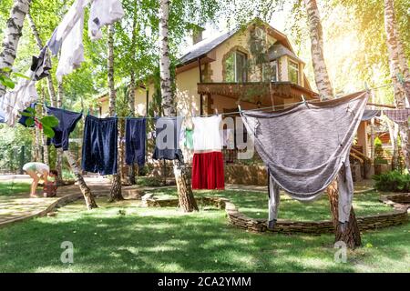 Domestic real life scene of many children and adult fresh clean washed clothes hanged on birch tree clothesline with pins. Home yard on bright sunny Stock Photo