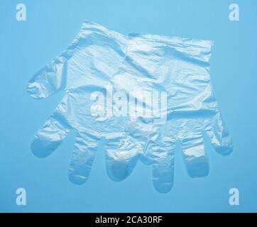 pair of disposable polyethylene gloves on a blue background, top view, flat lay.
