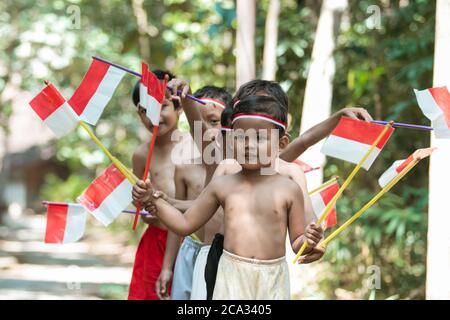 having fun group of kids walking without clothes when holding small the red and white flag and raised the flag against a tree background Stock Photo