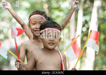 close up of children face when holding small red and white flag and raised together the flag on with lots of trees in the background Stock Photo