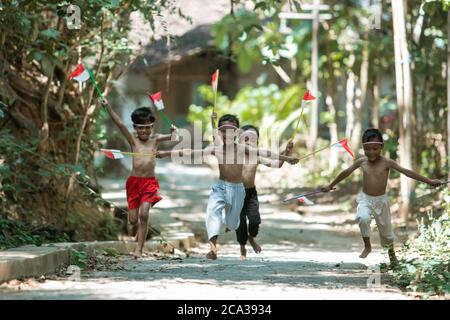 having fun group of kids running without clothes chasing each other when holding small the red and white flag and raised the flag against a tree background Stock Photo