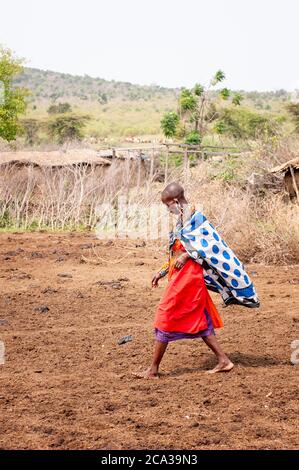 Maasai woman, wearing traditional attire, walking in a maasai village. Maasai Mara National Reserve. Kenya. Africa. Stock Photo