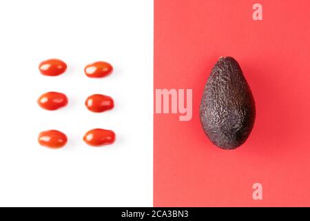 Avocado and cherry tomato on colorful red background. Pop art design, creative summer food concept. Healthy food minimal flat lay. Stock Photo