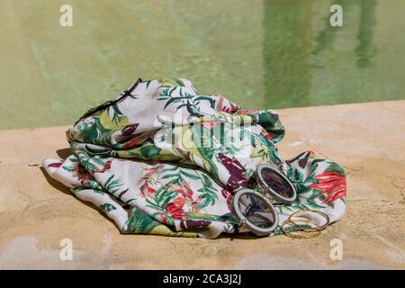 Sunglasses and tropical dress on the edge of a swimming pool. Summer concept with copy space.