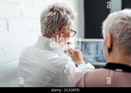 back view of two business woman discussing about project and looking at laptop screen Stock Photo
