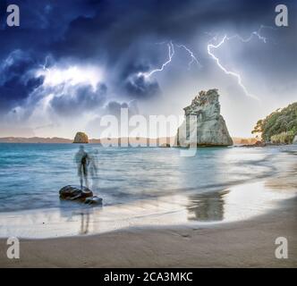 People silhouettes looking at Cathedral Cove marine reserve with storm approaching, Coromandel Peninsula,  New Zealand. Stock Photo