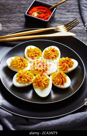 Picnic dish of hard-boiled eggs: deviled eggs filled with smashed egg yolks mustard, mayonnaise, white vinegar sprinkled with smoked paprika on a blac Stock Photo