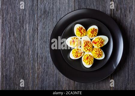 Easy keto recipe of deviled eggs filled with mustard, mayonnaise, white vinegar sprinkled with smoked paprika on a black plate  on a dark wooden backg Stock Photo
