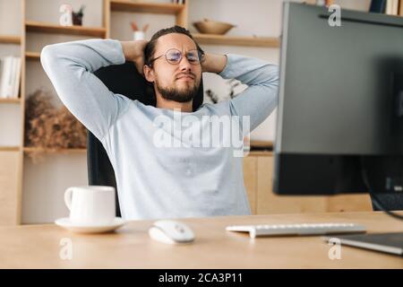 Image of unhappy bearded programmer man wearing eyeglasses working with computer in office Stock Photo